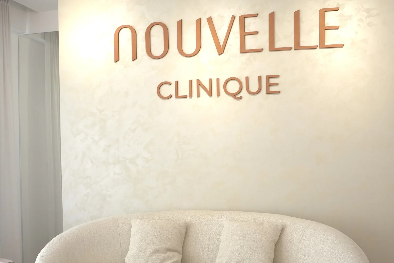 Sala d'attesa di Nouvelle Clinique a Tirana — logo a parete e divano